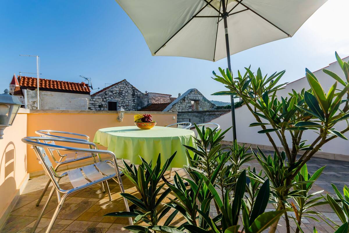 A terrace with a table and chairs, a bowl of fruit, and a large umbrella.