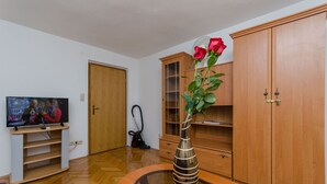 A living room with a TV, wooden cabinets, a glass coffee table, and a vase with a rose. - Apartments Old Town (Trogir)