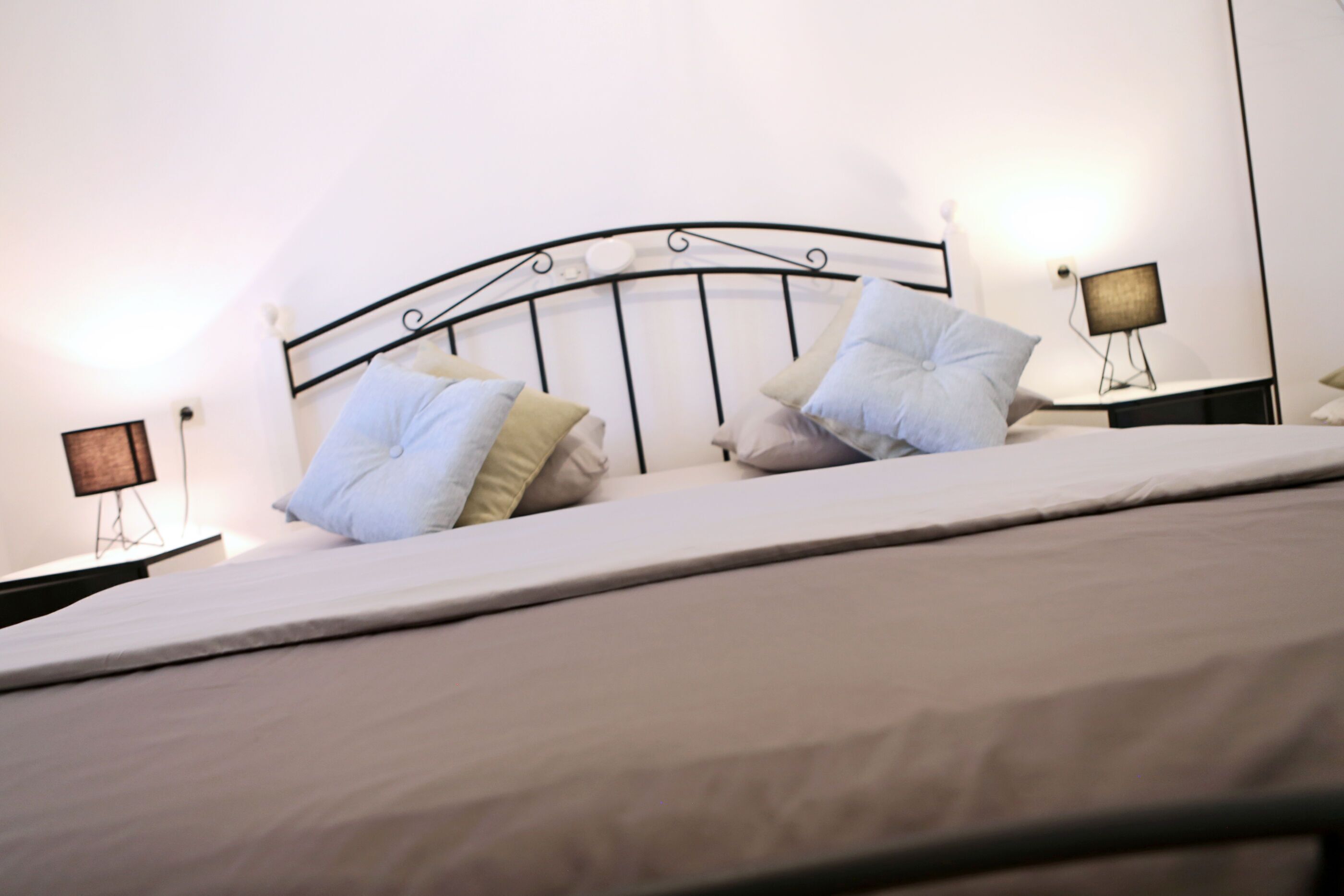 A neatly made bed with a metal headboard, two bedside tables with lamps, and a plain white wall.
