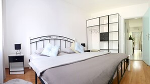 Ένα υπνοδωμάτιο με ένα κρεβάτι, κομοδίνα, μια ντουλάπα και μια πόρτα που οδηγεί σε ένα άλλο δωμάτιο.