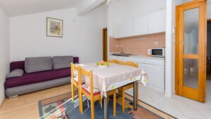 A compact living space with a dining table, chairs, a sofa, a kitchen area, and a door.