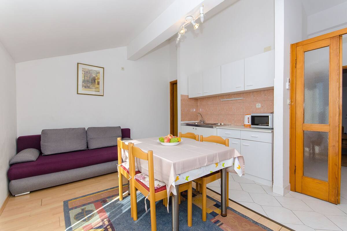 A compact living space with a dining table, chairs, a sofa, a kitchen area, and a door.