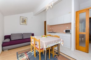 Un espace de vie compact comprenant une table à manger, des chaises, un canapé, un coin cuisine et une porte.