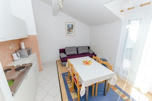 A compact living space with a kitchenette, a dining table with chairs, a sofa, and a window with curtains.