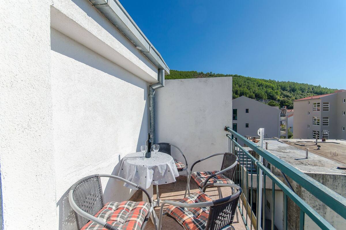 A balcony with a table and chairs, a view of buildings, and a clear sky.