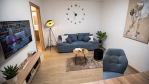 A living room with a large wall clock, a sofa, a coffee table, and a TV displaying a show. - Apartment N D (Sibenik)