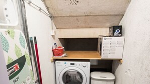 A compact laundry area with a washing machine, a drying basket, and a shelf with a box. - Apartment N D (Sibenik)