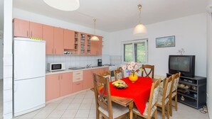 A compact kitchen with a dining area, white refrigerator, microwave, and wooden chairs. - Apartment Marija (Podstrana)