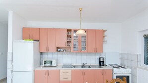 A compact kitchen with pink cabinets, a white refrigerator, a microwave, a stove, and a dining table with chairs. - Apartment Marija (Podstrana)