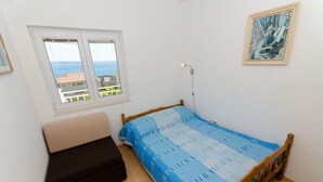 A bedroom with a bed, a bench, a window with a view, and a painting on the wall. - Apartment Marija (Podstrana)