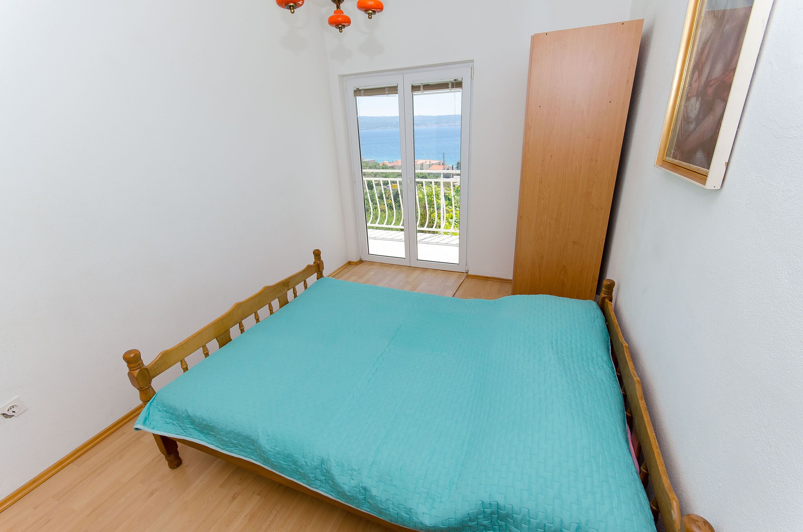 A bedroom with a bed, a balcony with a view of the sea, and a wooden door.