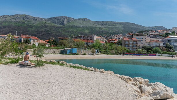 A coastal town with buildings, a beach, and a mountain in the background. - Apartment Mario (Strozanac)