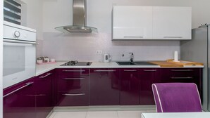 A modern kitchen with white cabinets, a stainless steel range hood, and a purple chair. - Apartment Mario (Strozanac)