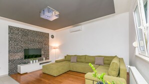 A modern living room with a sectional sofa, a flat-screen TV, a stone accent wall, and a potted plant. - Apartment Mario (Strozanac)