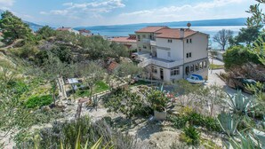 Un immeuble à plusieurs étages doté d’un balcon, entouré de verdure et offrant une vue sur la mer.