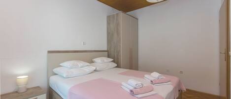 A bedroom with a wooden ceiling, a bed with white bedding, a bedside table with a lamp, and a wardrobe.
