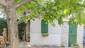 A rustic building with a stone facade, green shutters, and a tree in the foreground. - Apartments Romic (Jadrija)