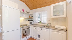 A compact kitchen with white cabinets, a gas stove, a microwave, and a sink. - Apartments Romic (Jadrija)