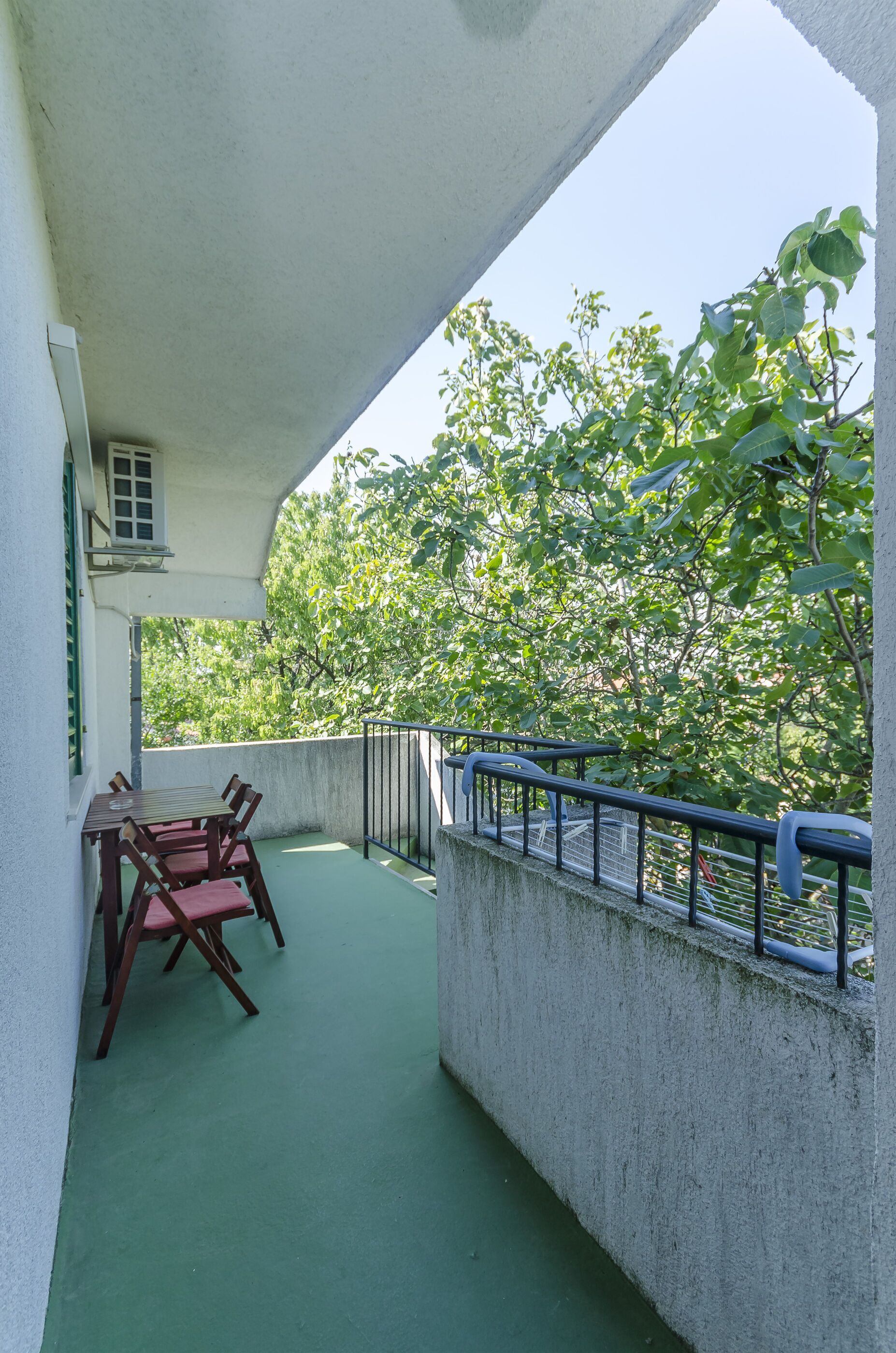 Ein Balkon mit grüner Bodenfläche, einem Tisch mit Stühlen und einem Geländer.