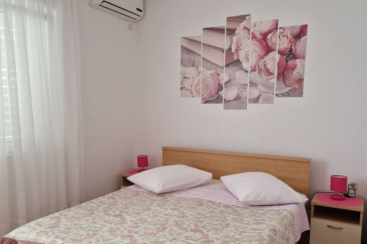 Une chambre à coucher avec un lit en bois, une table de chevet rose, une lampe rouge et un climatiseur fixé au mur.