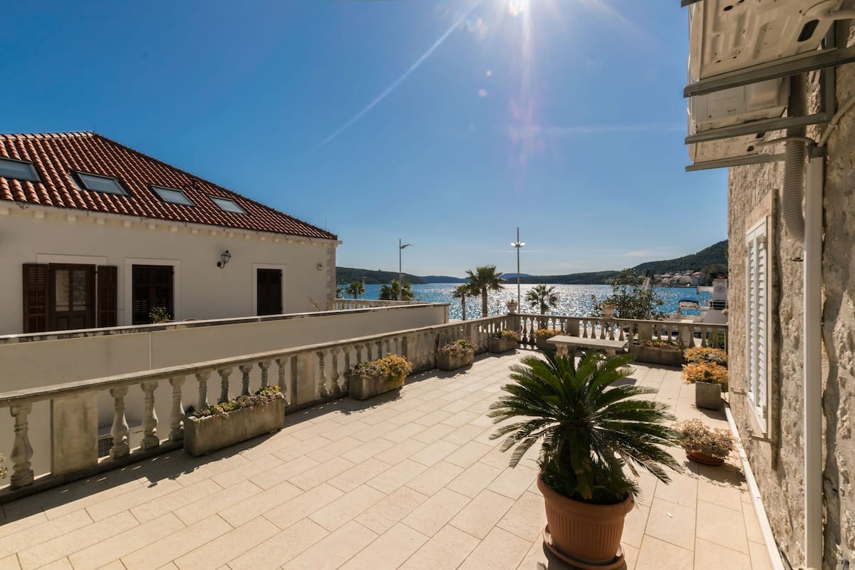 A terrace with tiled flooring, potted plants, and a view of the sea.