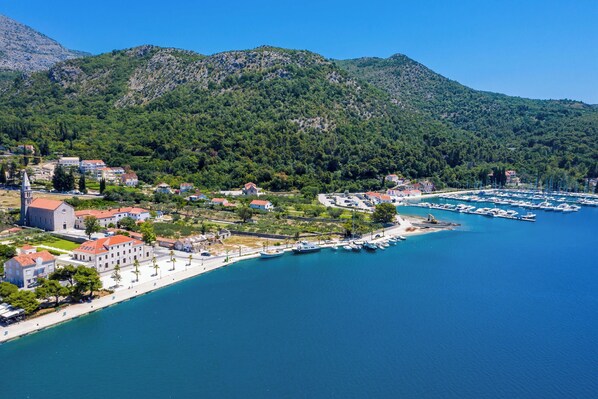 A coastal town with a marina, buildings, and a mountainous backdrop.