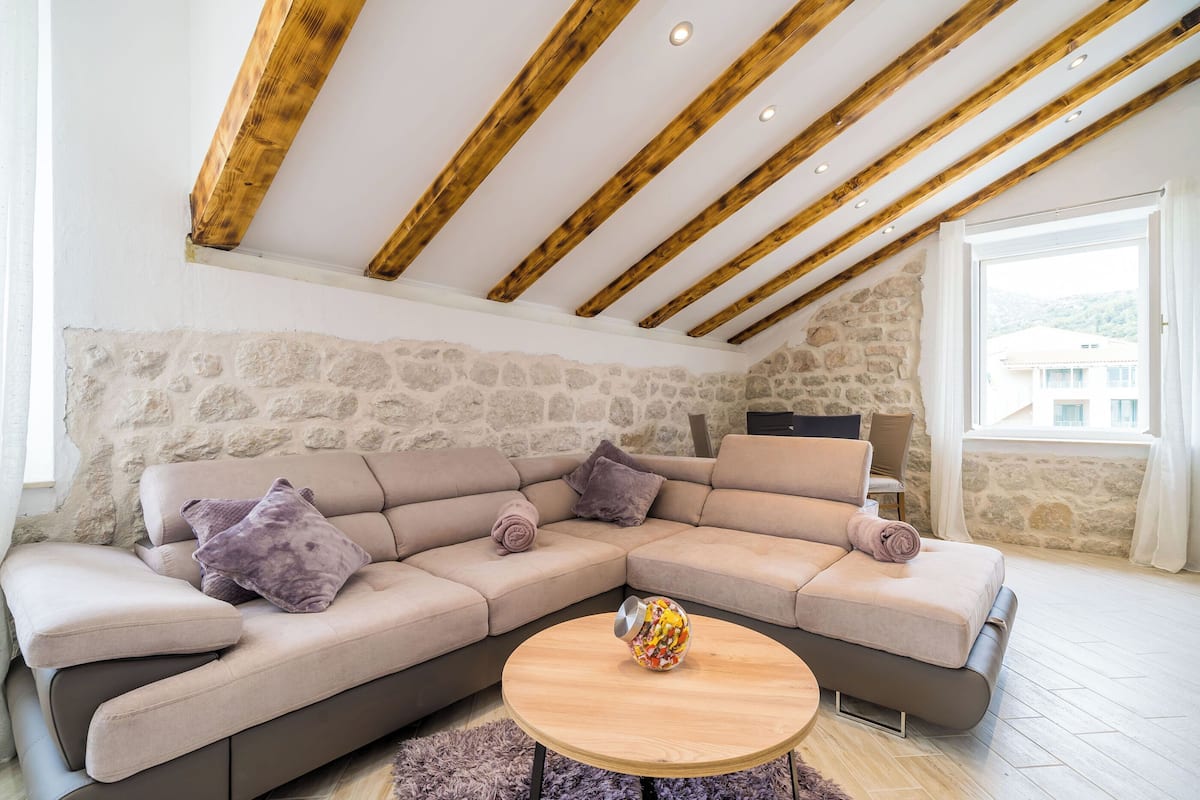 A modern living room with a sectional sofa, a round wooden coffee table, and exposed wooden beams on the ceiling.