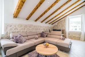 Un salon moderne avec un canapé d’angle, une table basse ronde en bois et des poutres apparentes en bois au plafond.