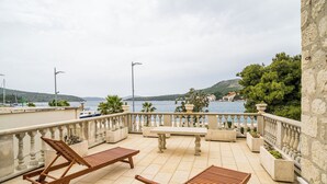 Eine Terrasse mit Holzliegen und einem Tisch, mit Blick auf ein Gewässer und Hügel.