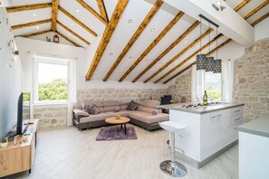 A modern interior with a stone wall, wooden beams, a sofa, a dining area, and a kitchen.