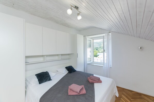 A bedroom with a bed, white walls, a wooden ceiling, and a window with a view. - Apartments Davor (Slano)
