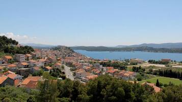 A coastal town with red-roofed buildings, a clear blue lake, and hilly terrain in the background.