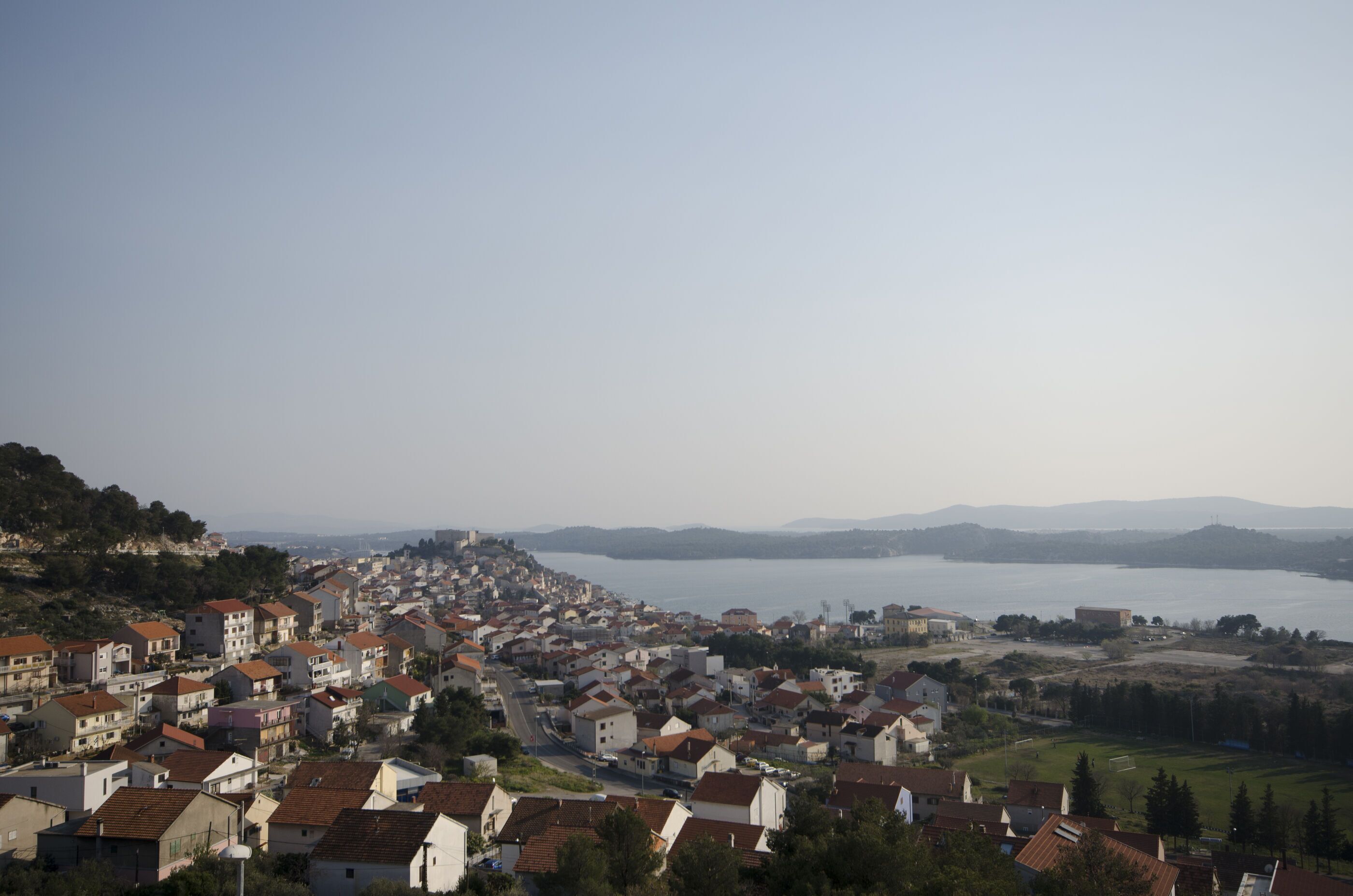 A coastal town with a view of the sea and distant mountains.