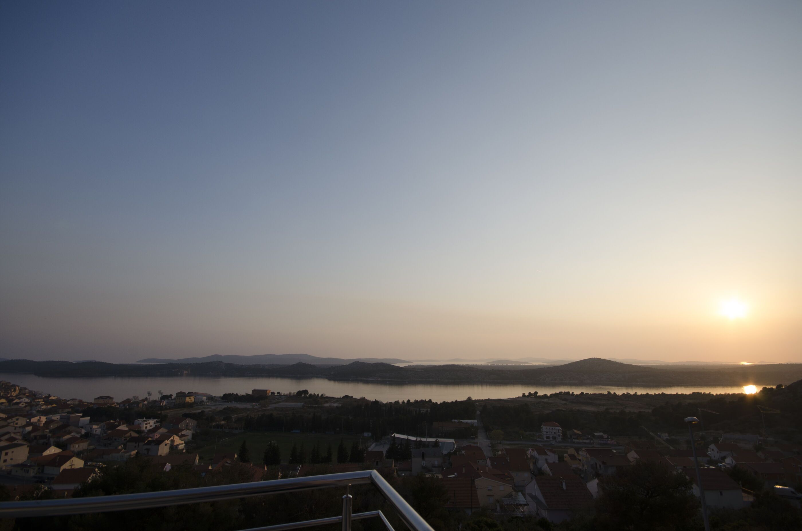 A panoramic view of a lakeside town at sunset with visible buildings and hills in the background.