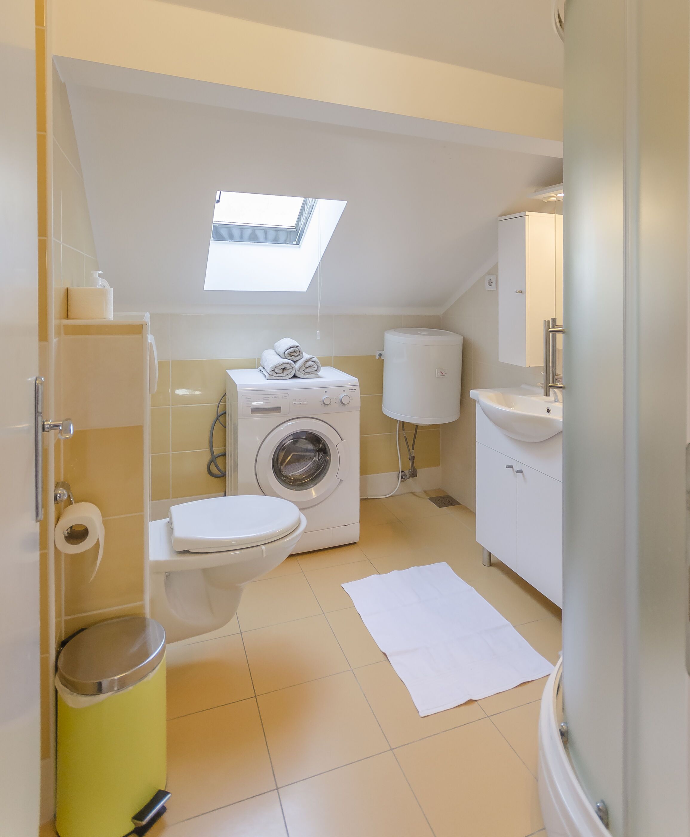 Een compacte, moderne badkamer met dakraam, een wasmachine, toilet en wastafel.
