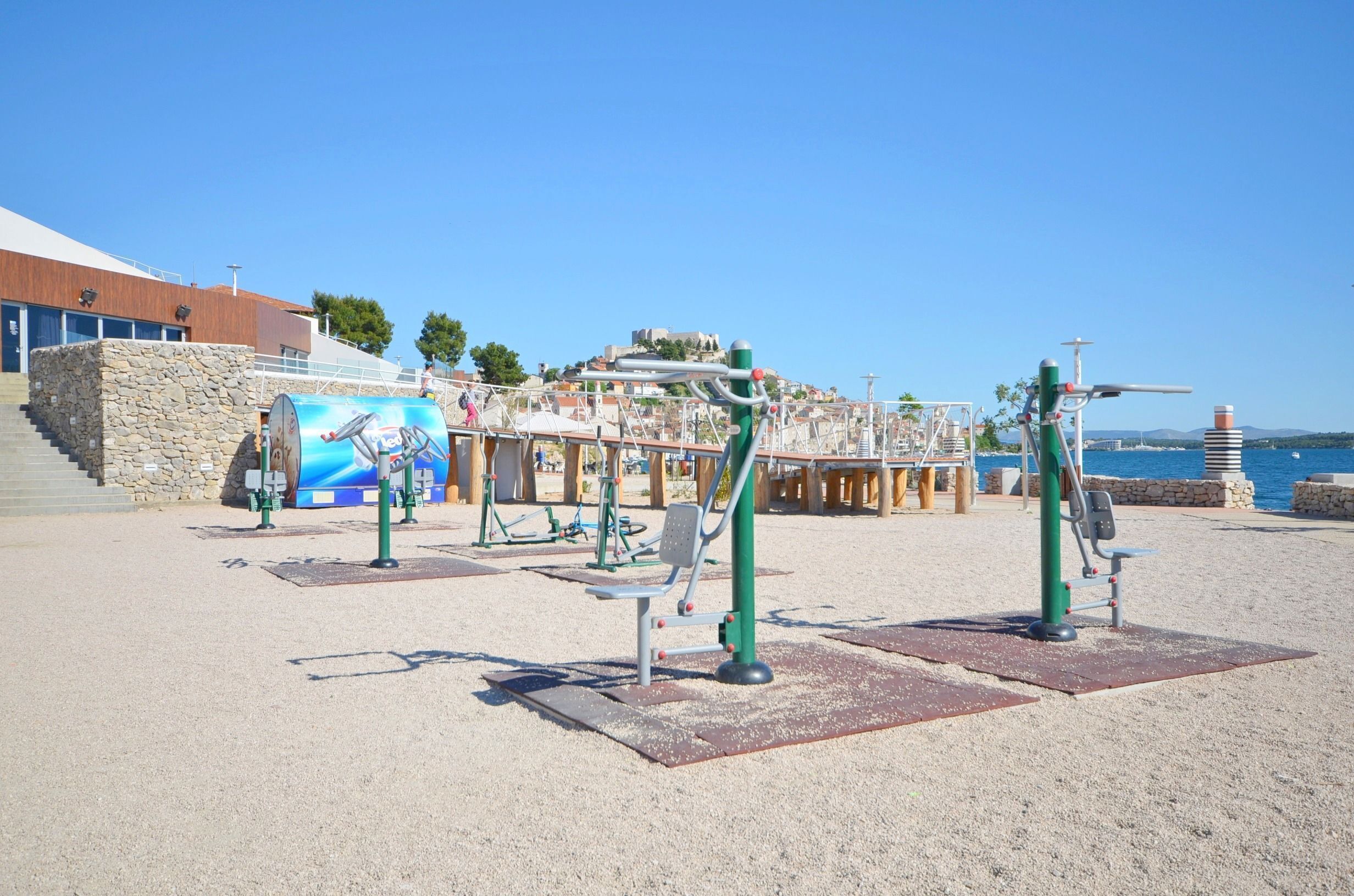 Een buitenfitnessruimte met trainingsapparatuur, een stenen muur en uitzicht op zee.