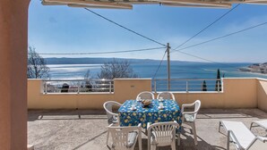 Ein Balkon mit Tisch und Stühlen, der Blick auf die Küste freigibt.