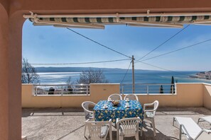 Ein Balkon mit Tisch und Stühlen, der Blick auf die Küste freigibt.