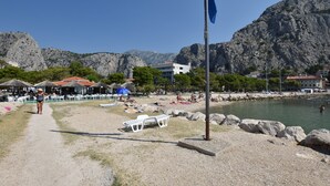 Ein Strand mit felsigem Hintergrund, ein Pfad zum Wasser und eine Fahnenmasten.