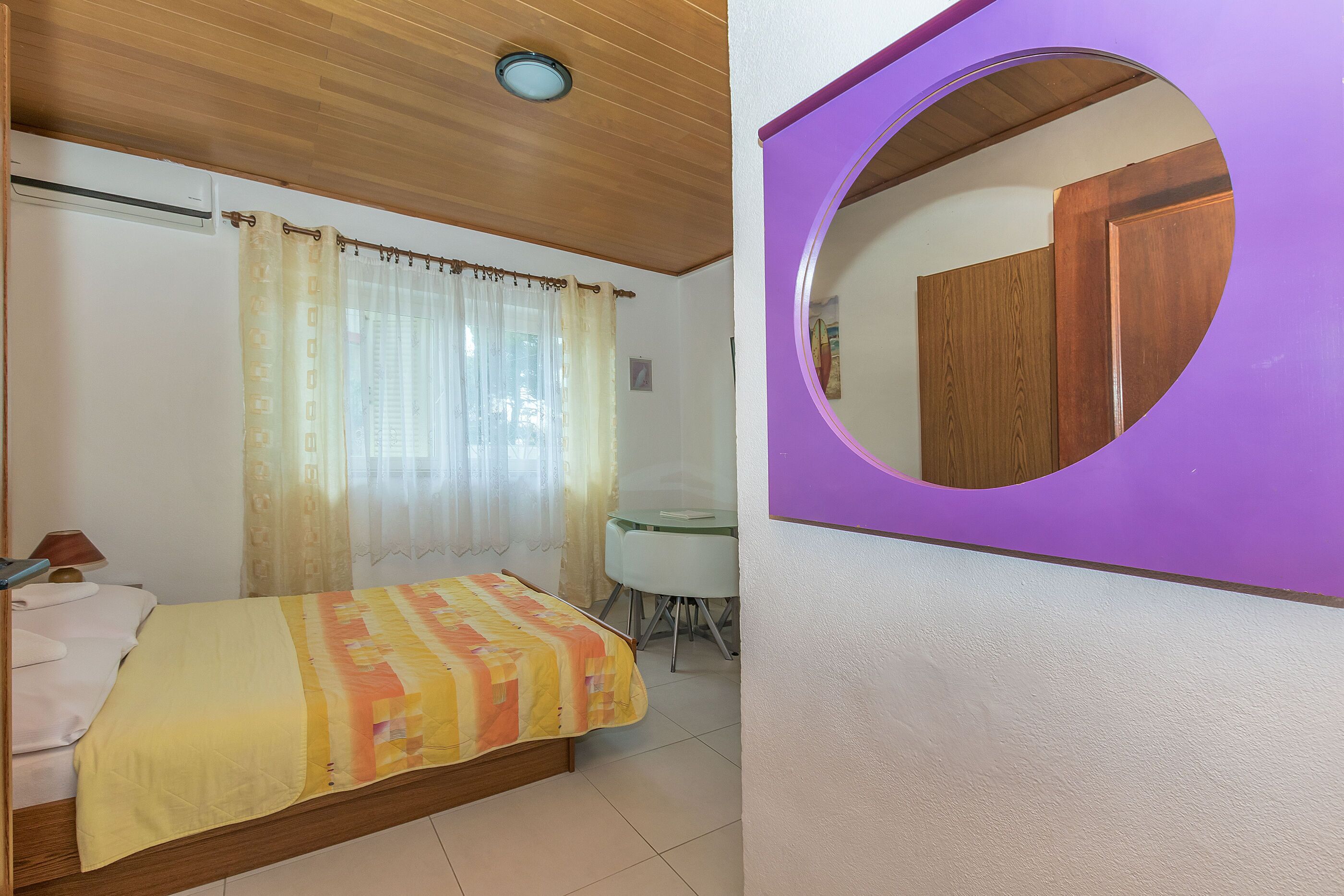 A bedroom with a bed, a desk, and a mirror.