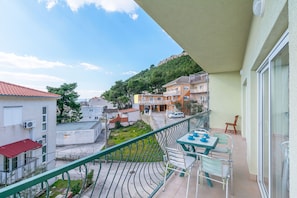 Ein Balkon mit Tisch und Stühlen, der auf eine Straße mit Gebäuden und einen Hügel blickt.