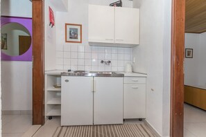 Eine kleine Küche mit weißen Schränken, einer Edelstahl-Spüle und einem kleinen Kühlschrank.