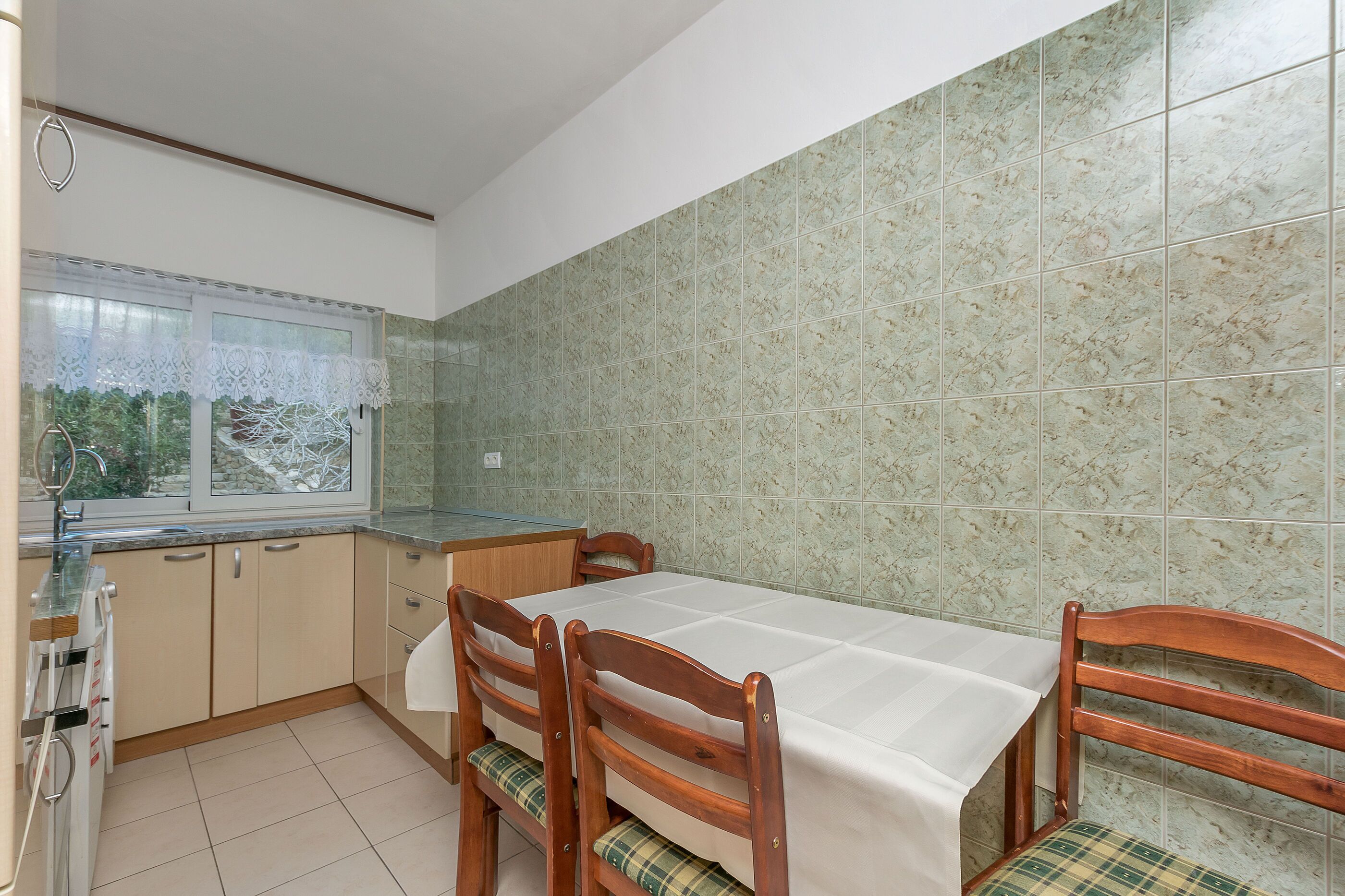 A kitchen with a dining table, chairs, and a window with a lace curtain.
