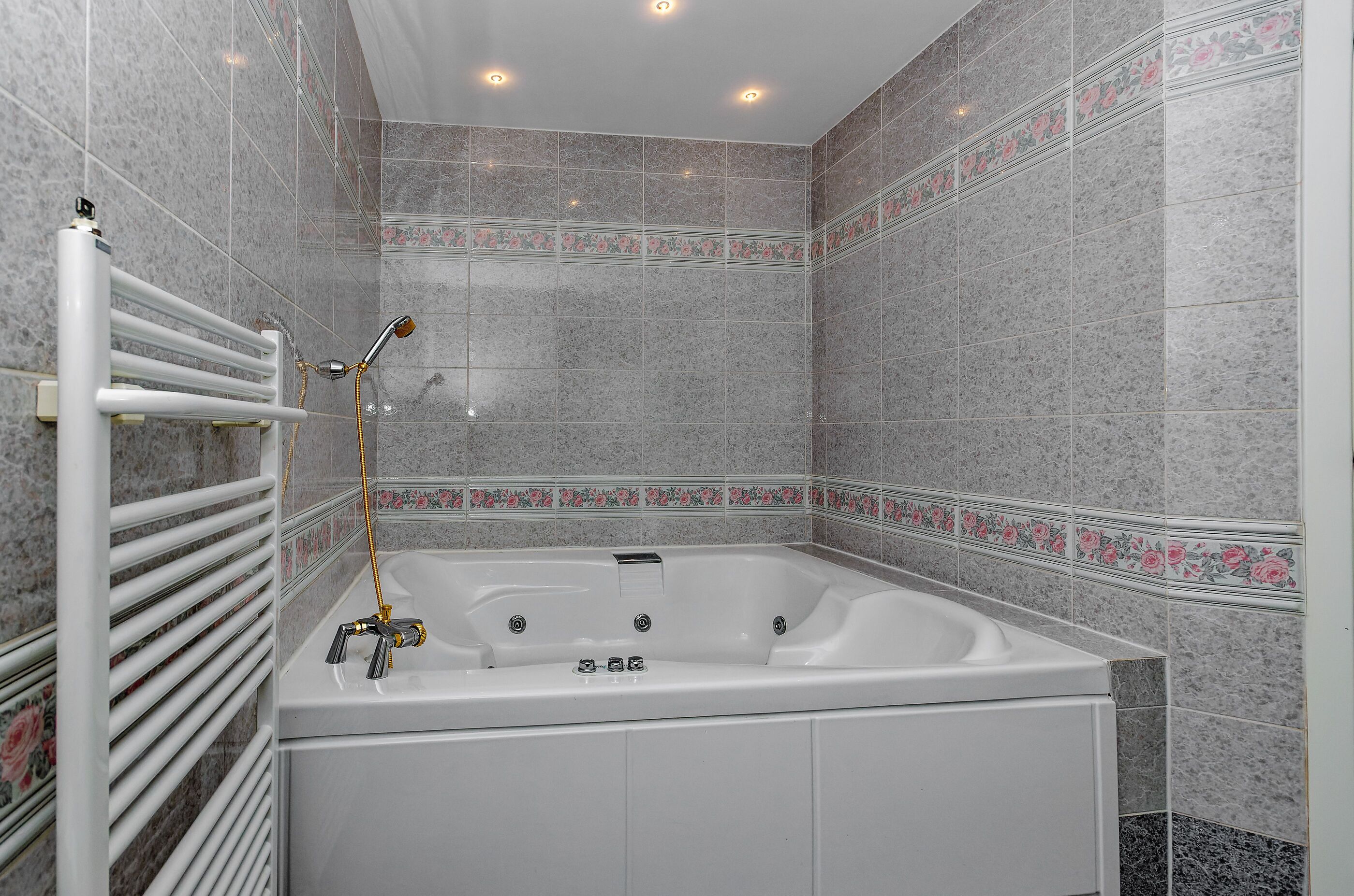 A modern bathroom with a large bathtub, a white towel rack, and a showerhead.