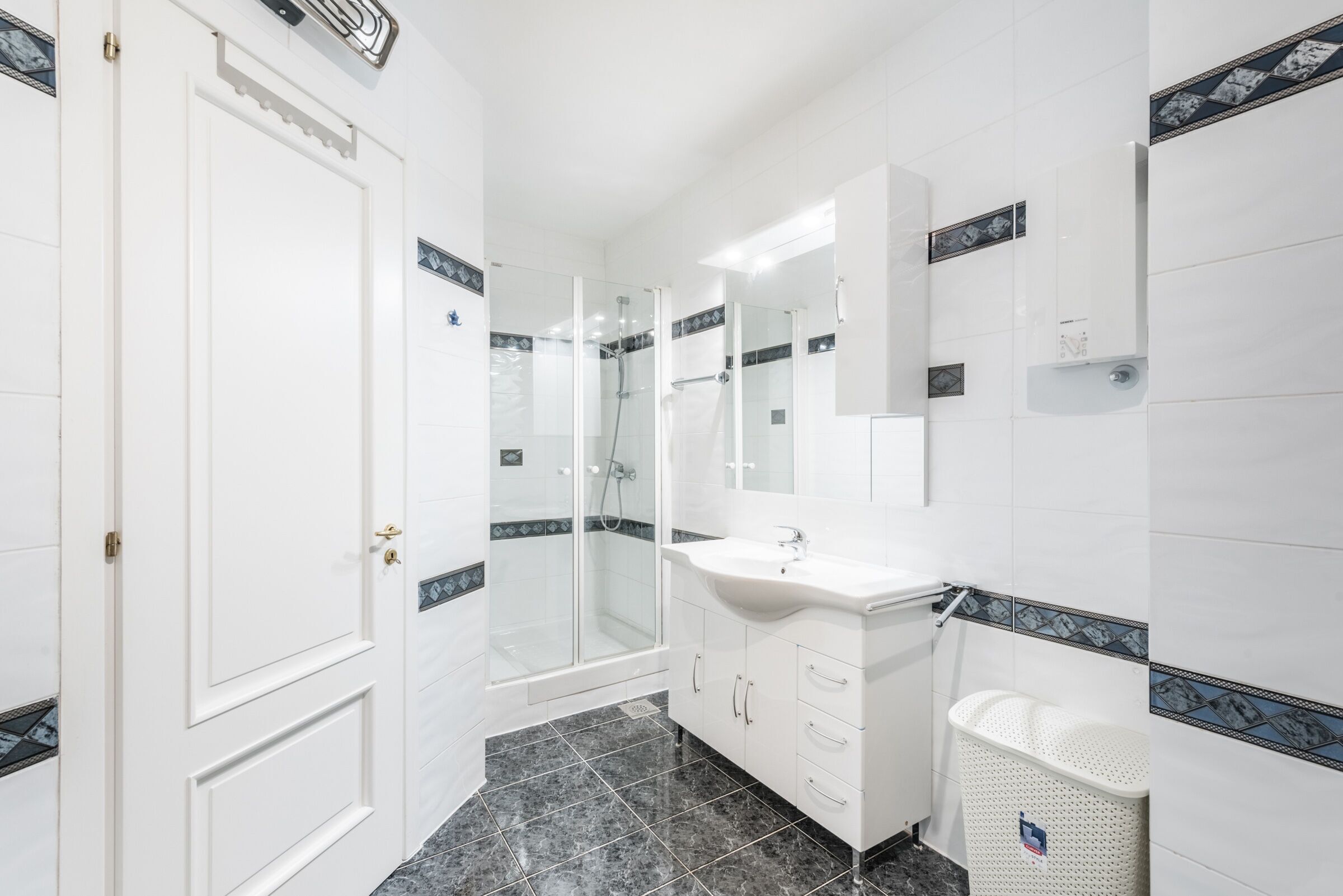Een moderne badkamer met een glazen douchecabine, een wit wastafelmeubel en een witte wasmand.