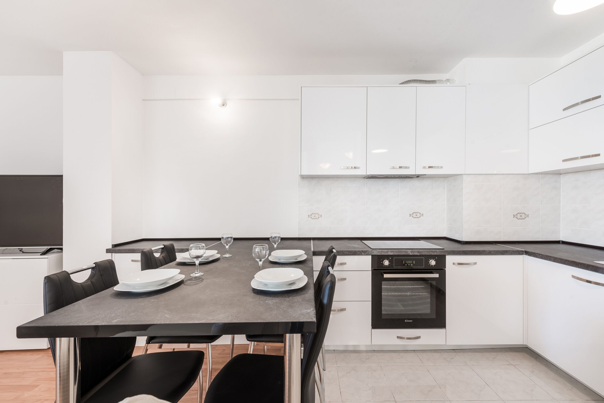 A modern kitchen with white cabinets, a black countertop, and a dining table set with plates and glasses.