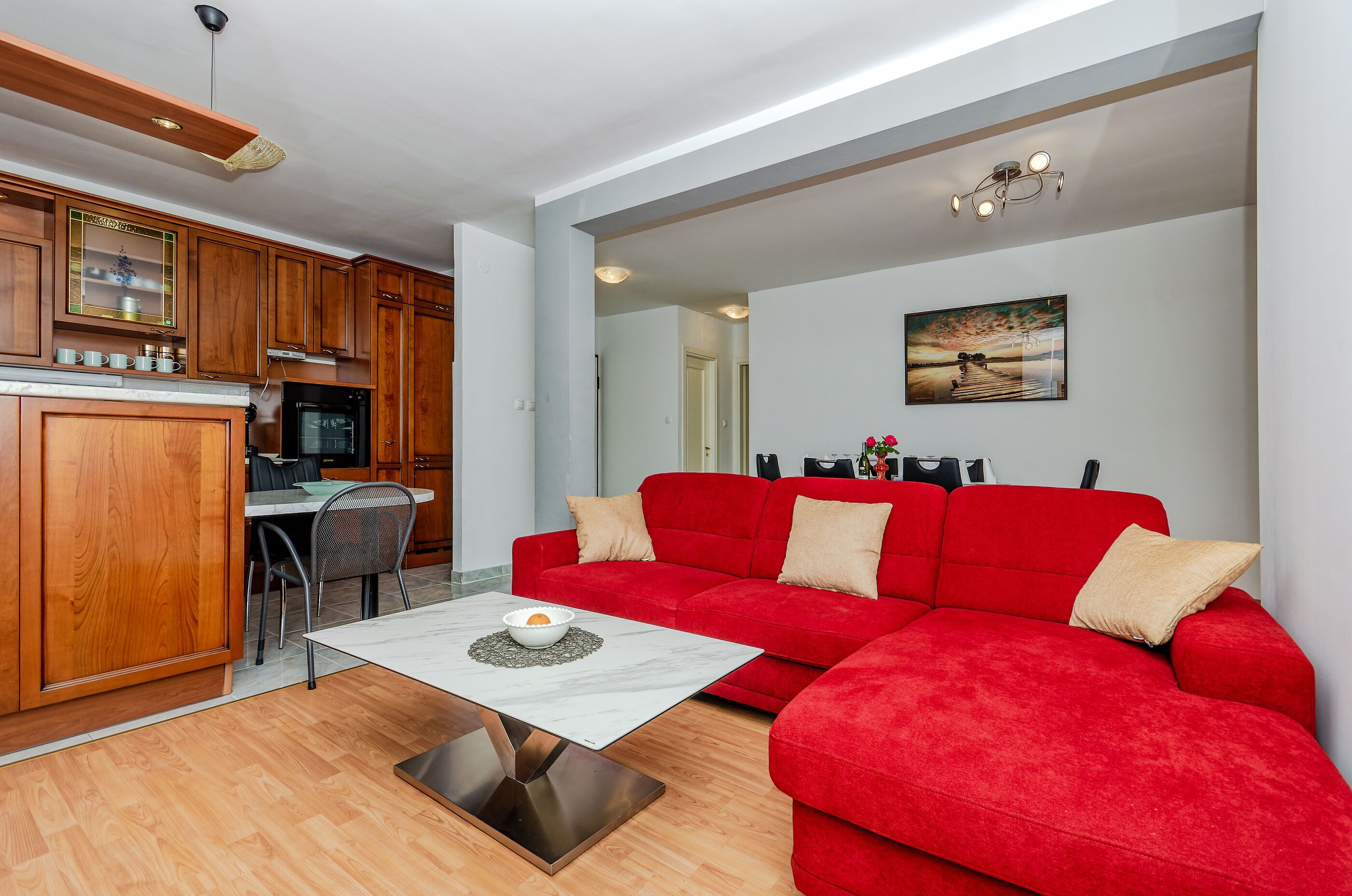 Una sala moderna con un sofá rojo, una mesa de comedor y una zona de cocina con armarios de madera.