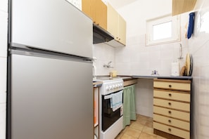 Une cuisine avec un réfrigérateur blanc, une cuisinière, des armoires en bois, une fenêtre et un dosseret carrelé.