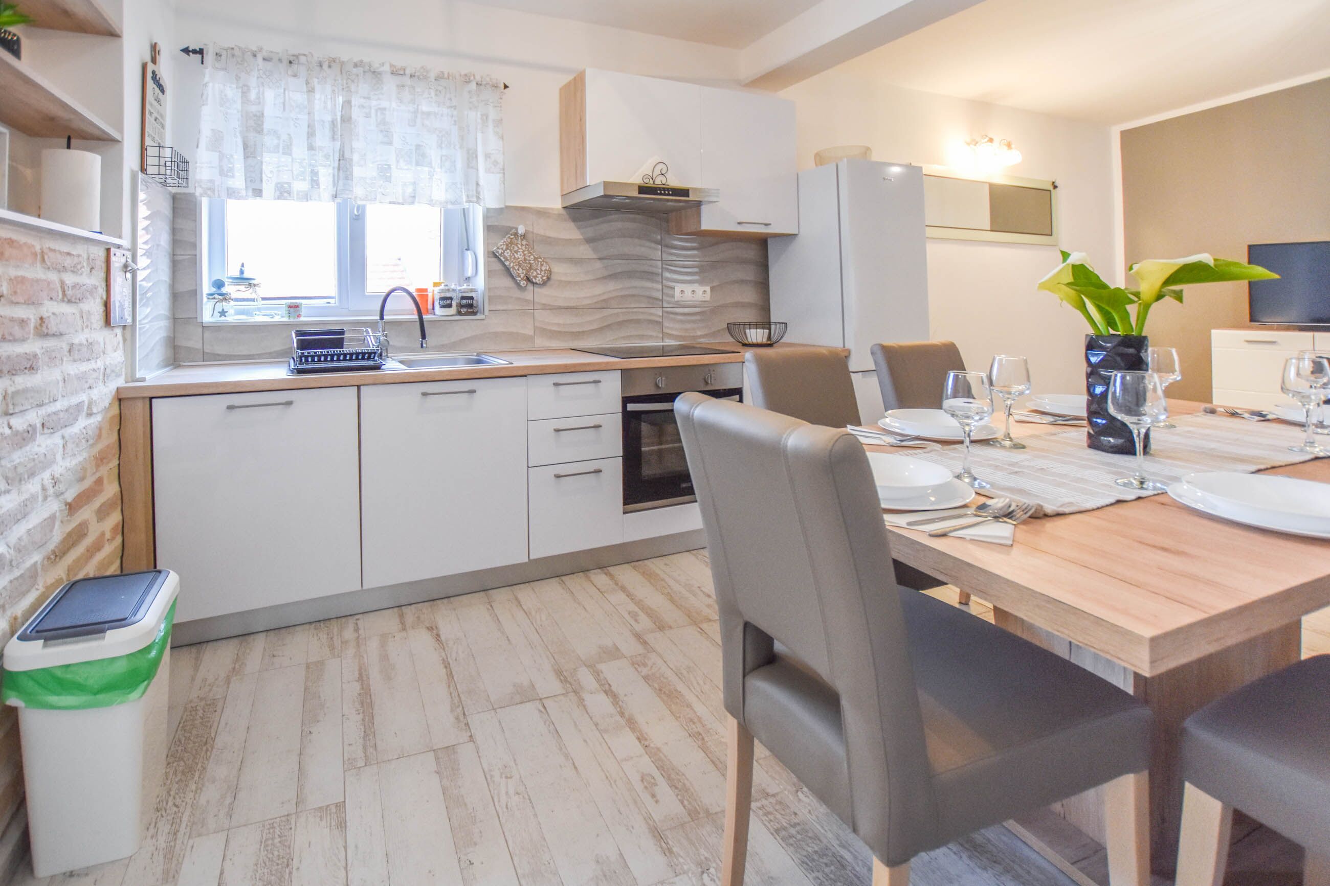 A modern kitchen with white cabinets, a built-in oven, and a window with curtains.