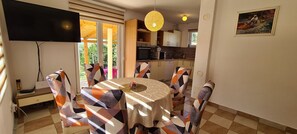 Enjoy meals in this dining area with a round table and six chairs, a flat-screen TV, and a kitchen in the background.